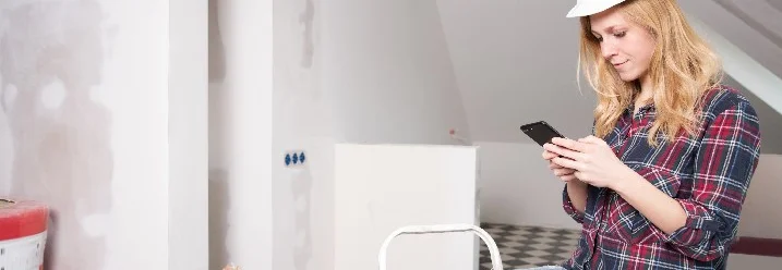 Person mit Helm und Handy in einem Rohbau